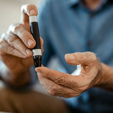 Person using a pen-like device to check blood sugar levels on their fingertip.