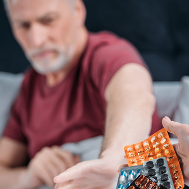 An elderly man reaching out for a blister pack of medication being offered by another person.