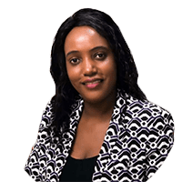A woman with long black hair wearing a patterned black and white blazer, smiling and looking directly at the camera.